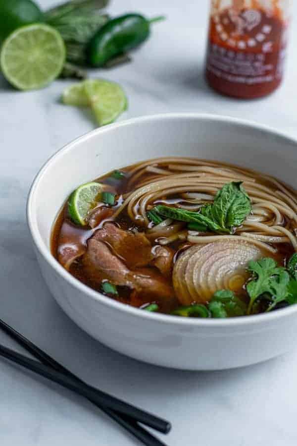 bowl of beef pho made in the slow cooker covered in green garnishes are ready to eat