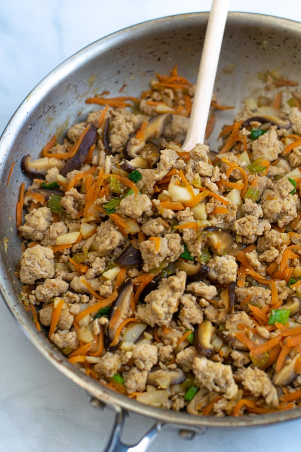 the chicken filling for the lettuce wraps in a skillet with a wooden spoon