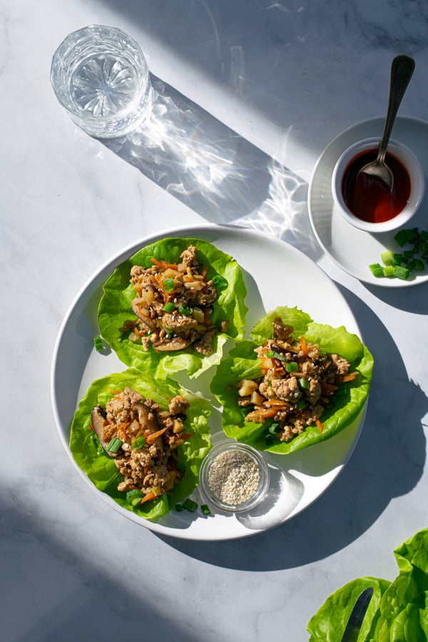 overhead shot of a plate with 3 chicken wraps along with a glass of water and bowl of sriracha 