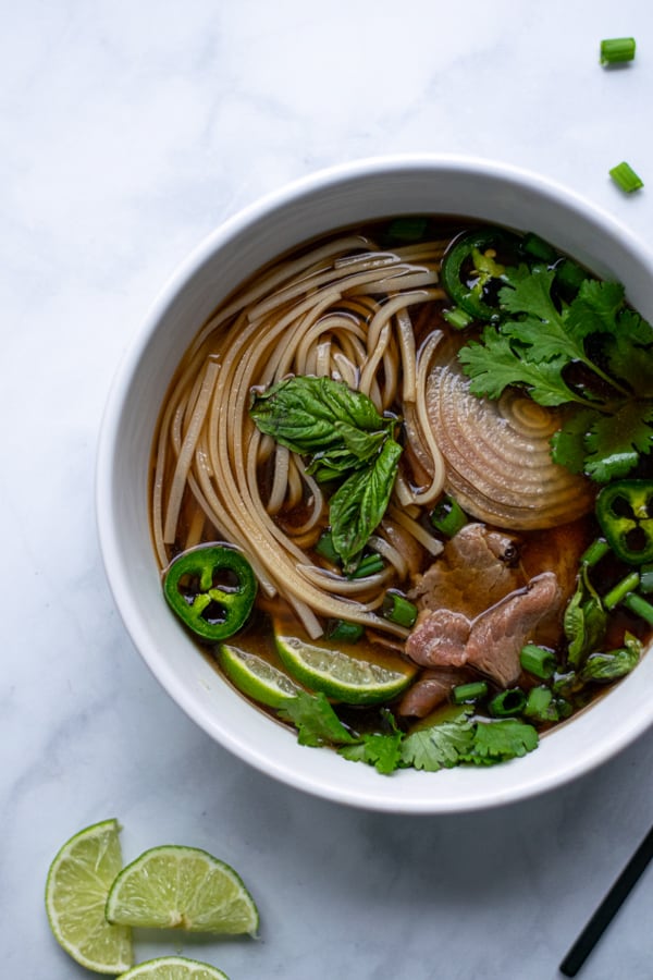 green garnishes cover a large bowl of beef pho