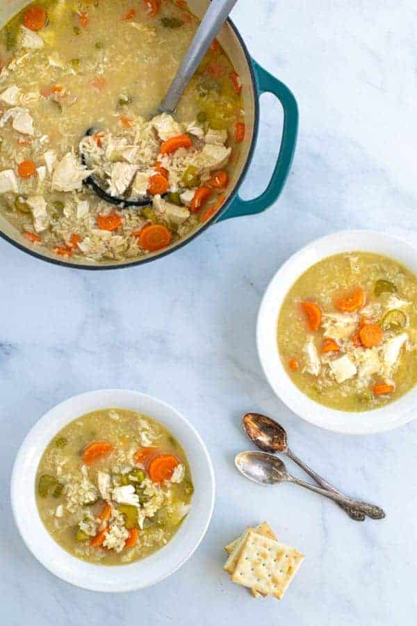 two bowls and a pot full of chicken and rice soup with spoons and crackers
