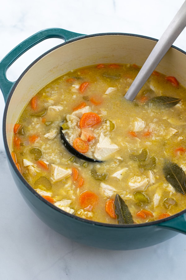 large blue dutch oven filled with freshly made chicken rice soup with a ladle