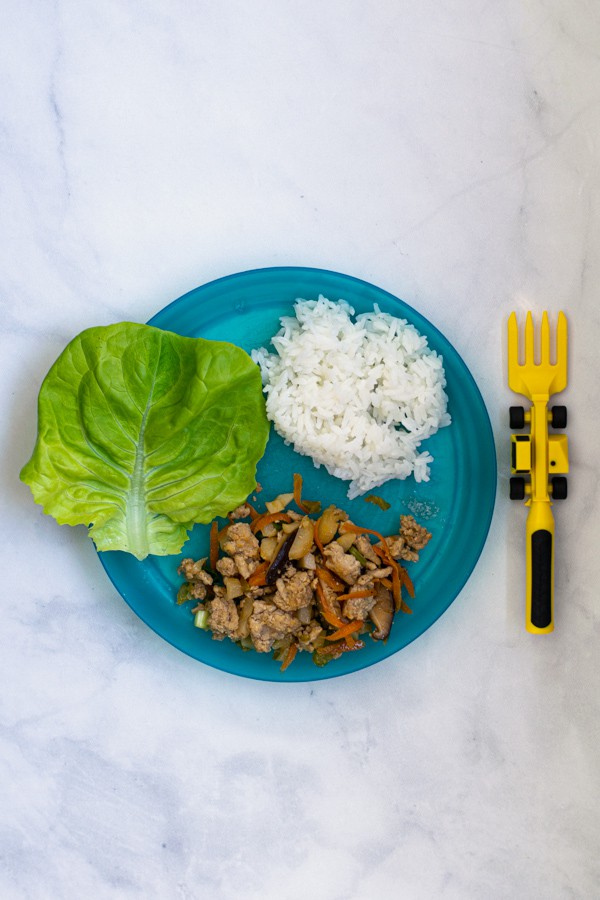 a blue kids plate with a construction truck fork with a kid size serving of asian chicken wraps