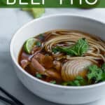 white bowl of beef pho made in the slow cooker with green garnishes