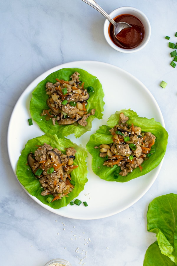 plate with three ground chicken lettuce wraps with a bowl of sriracha