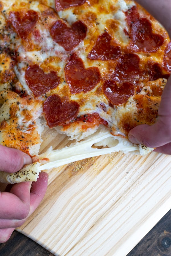 warm mozzarella stuffed pizza crust being pulled apart showing a long cheese pull
