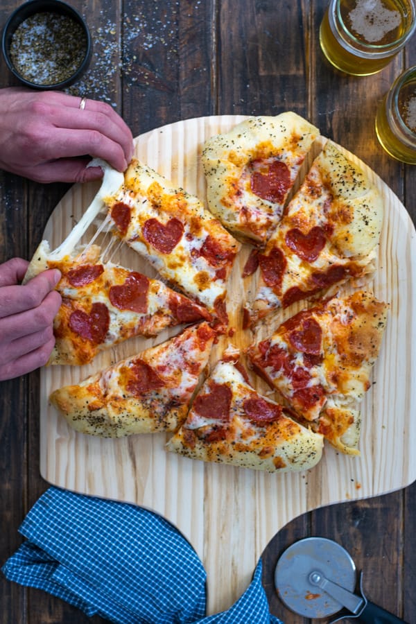 the pizza cut into pieces with hands puling apart a stretch of cheese between two slices