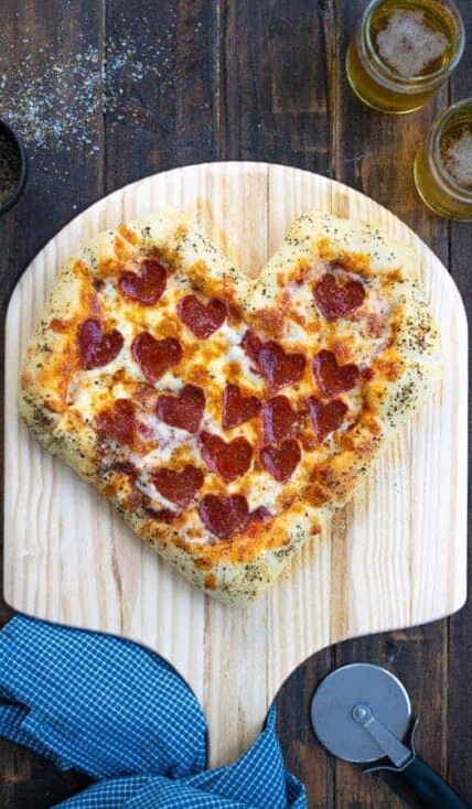 a freshly baked heart shaped pizza on a pizza paddle with heart shaped pepperoni