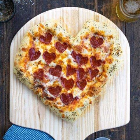 a freshly baked heart shaped pizza on a pizza paddle with heart shaped pepperoni