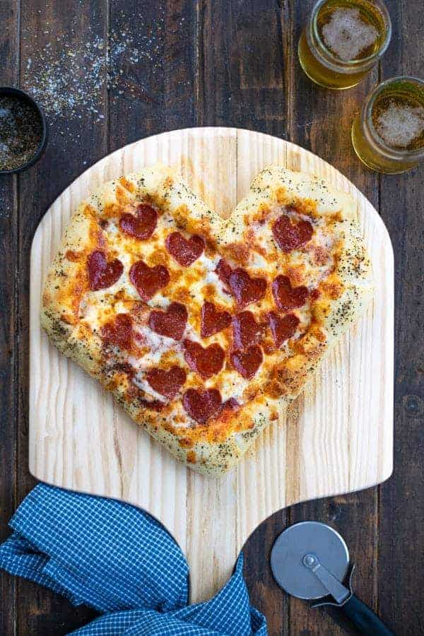 a freshly baked heart shaped pizza on a pizza paddle with heart shaped pepperoni