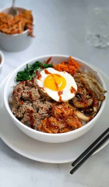 korean bibimbap bowl sitting on a table with chopsticks and kimchi