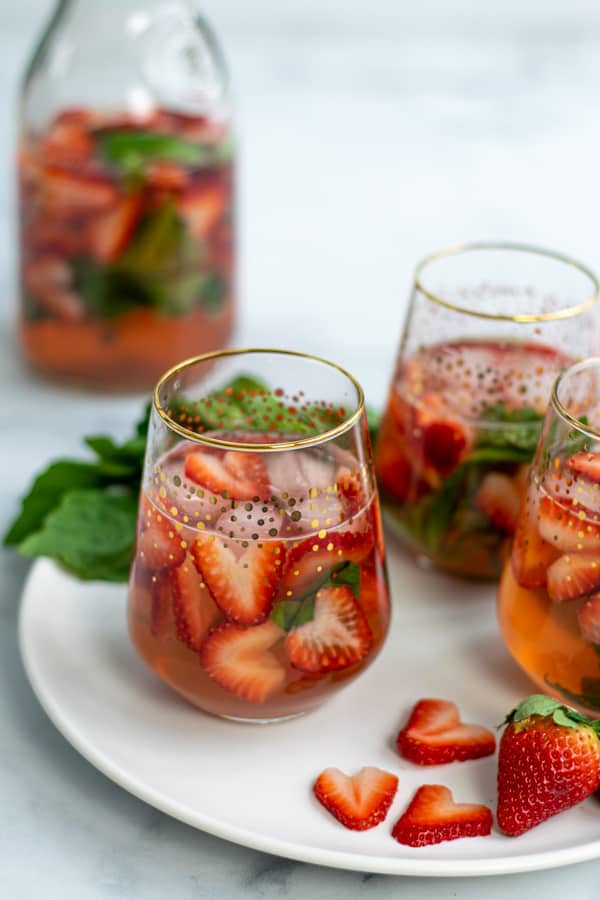 threes glasses of strawberry sangria on a plate with cut strawberries and basil