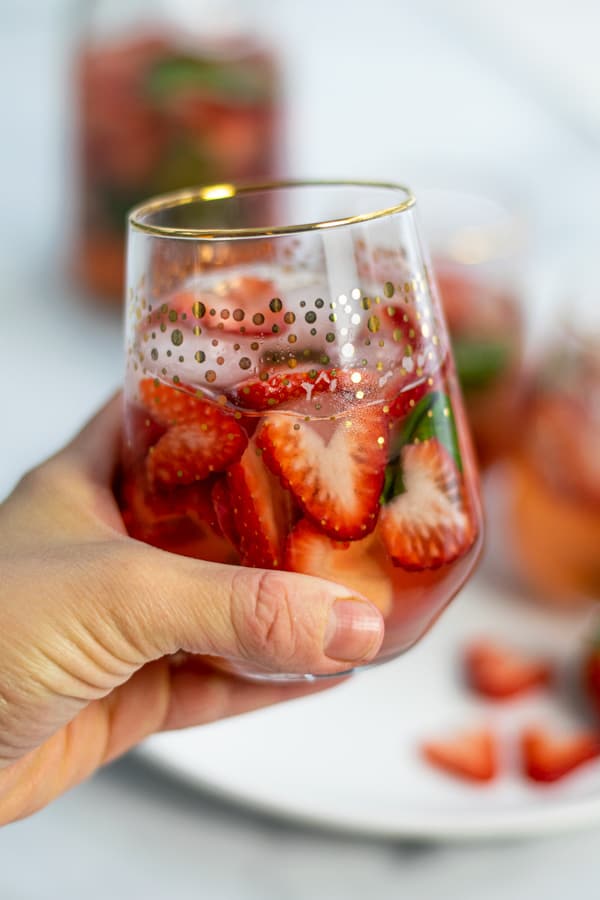 a hand holding a glass of strawberry basil sangria made with rosé wine