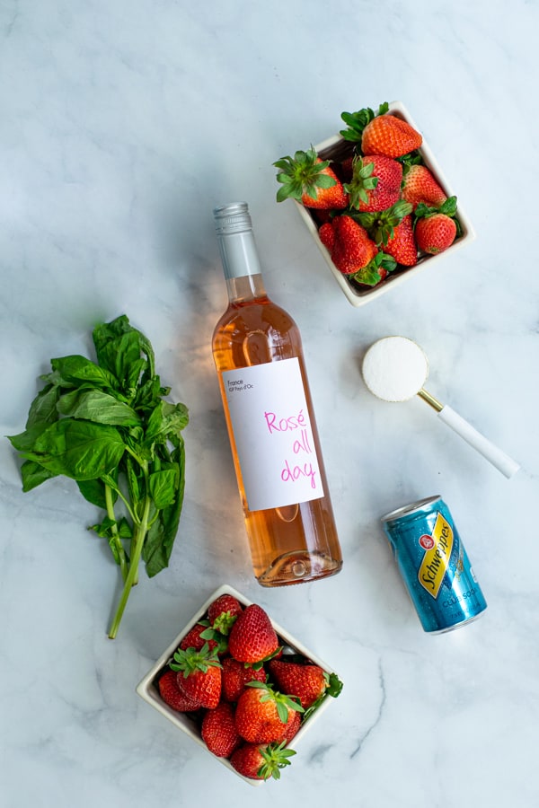 ingredients for strawberry sangria, rosé wine, strawberries, sugar, basil, and club soda