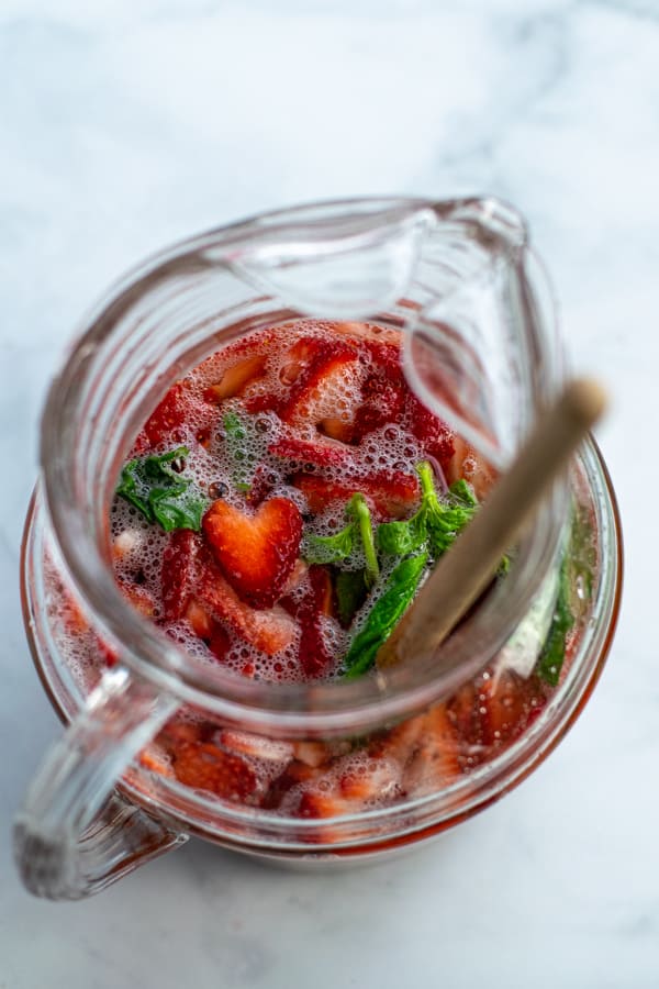 pitcher of sangria with basil and a sliced strawberry heart