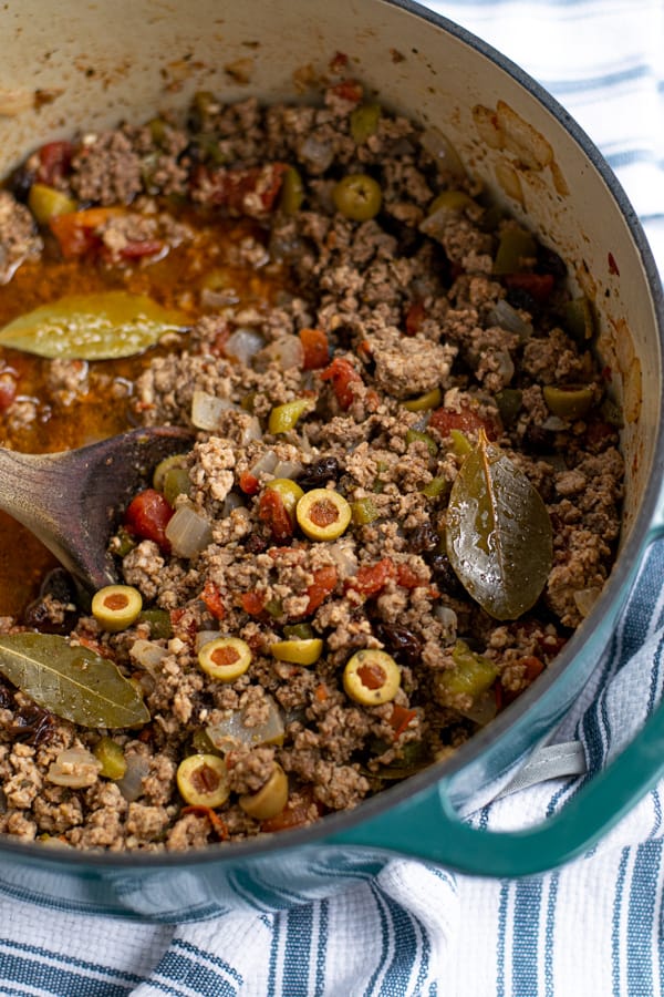 Picadillo in a dutch oven with a wooden spoon and bay leaves