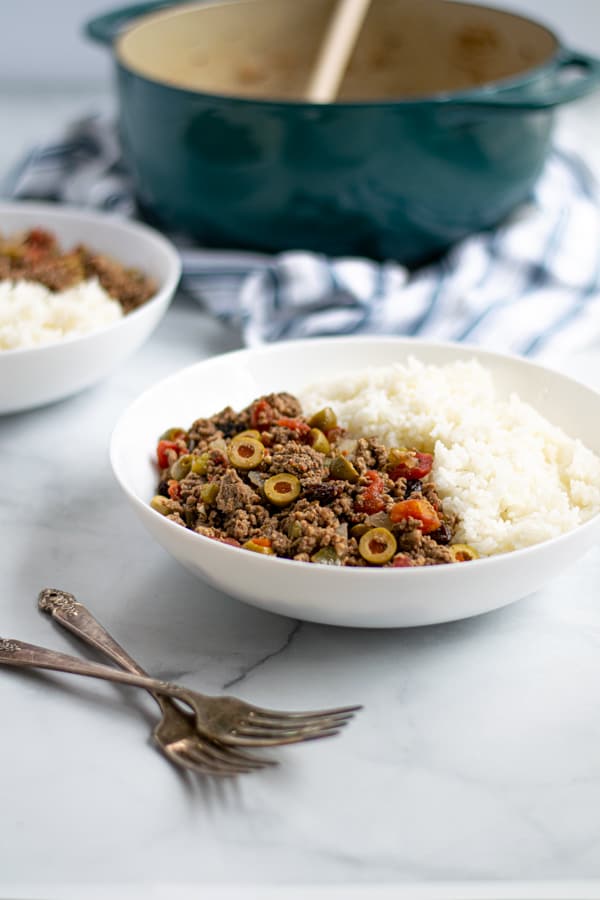 white bowl filled with rice and cuban picadillo full with tomatoes, olives, and raisins