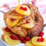 Pinterest pin with descriptions and glaze being poured over a spiral ham with pineapple slice