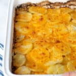 Pinterest Pin showing hands with towels holding a freshly made casserole full of Au Gratin Potatoes