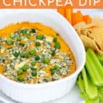 easy Buffalo Chickpea Dip in a small white baking dish with blue cheese and green onions with chips and vegetables for serving