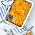 homemade au gratin potatoes in a white casserole dish with a some on a plate next to it with the title of the recipe