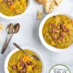 a pinterest pin with 3 bowls of split pea soup on a table with spoons and bread rolls