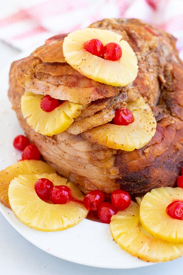 an easter ham on a white platter with pineapple rings and maraschino cherries for garnish 