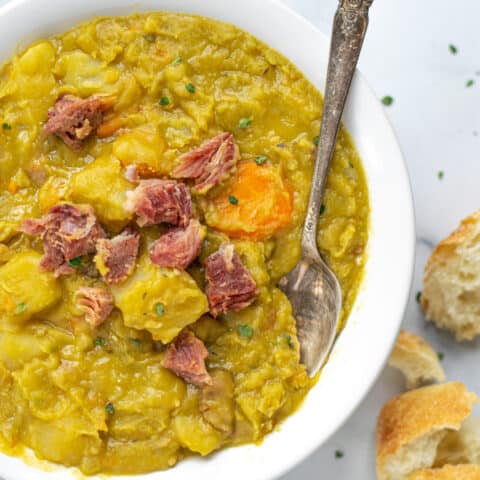 a bowl of split pea soup on a table with a roll