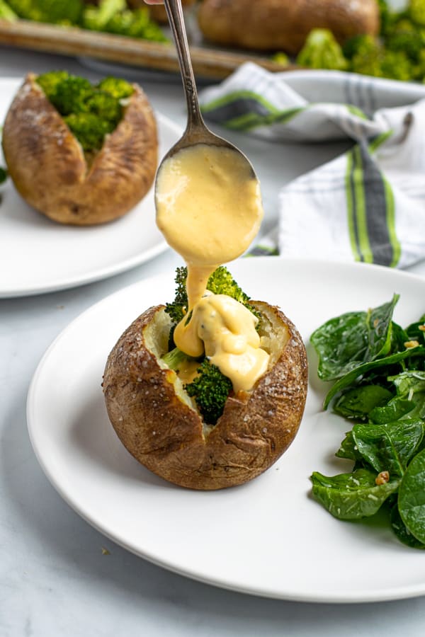 cheese sauce being fired over a baked potato stuffed with broccoli