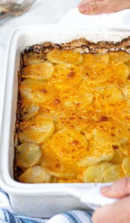 hands with towels holding a freshly made casserole full of Au Gratin Potatoes