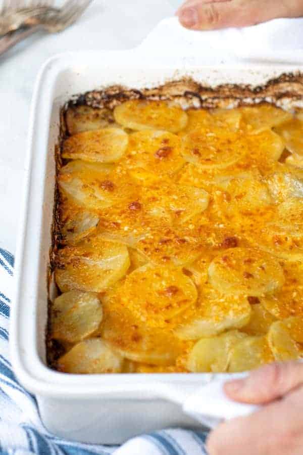 hands with towels holding a freshly made casserole full of Au Gratin Potatoes