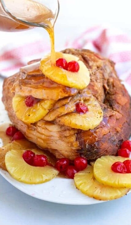 glaze being poured over a spiral ham with pineapple slice