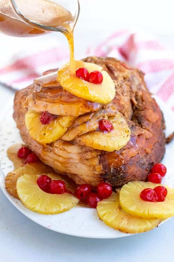 glaze being poured over a spiral ham with pineapple slice