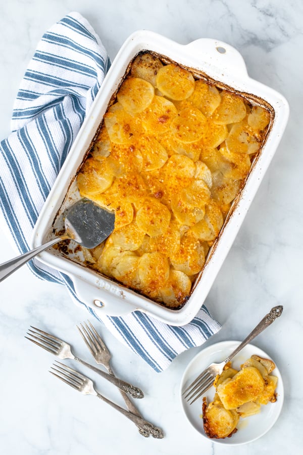 homemade au gratin potatoes in a white casserole dish with a some on a plate next to it