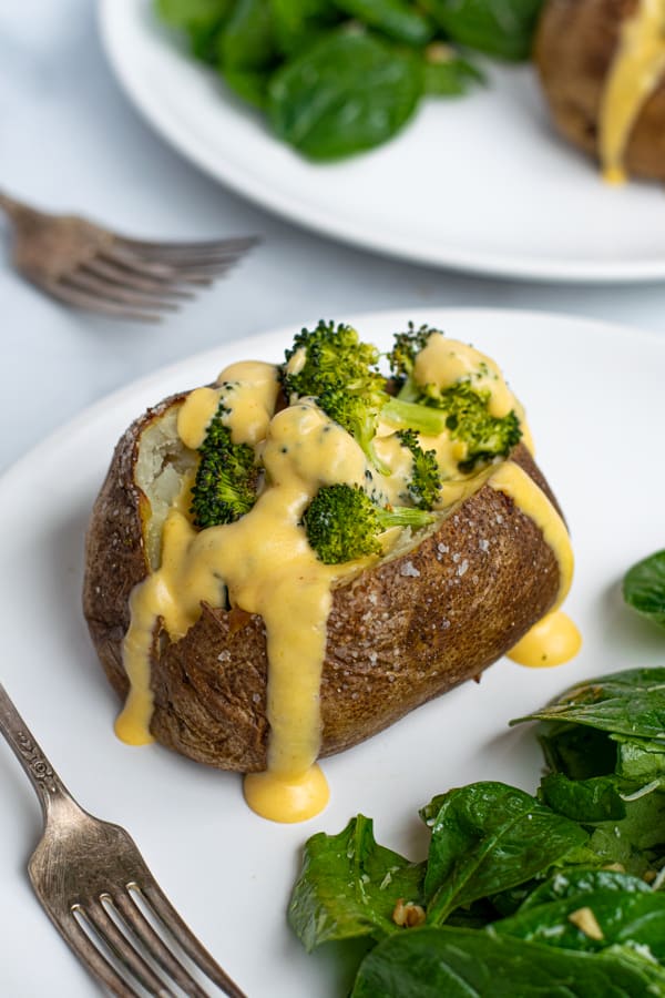 broccoli stuffed inside a baked potato topped with a creamy cheese sauce on a plate