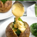 a baked potato stuffed with broccoli with a spoon dripping cheese sauce over the broccoli