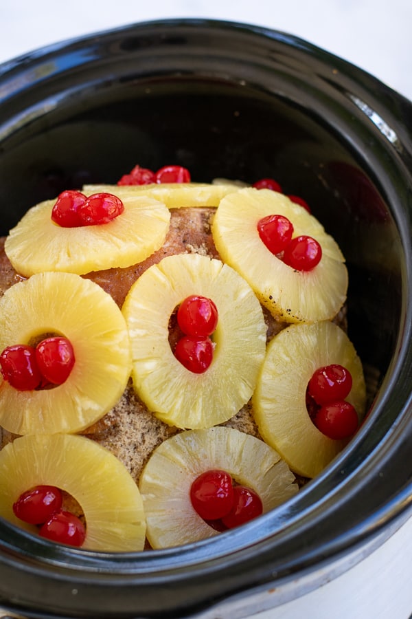 pineapple slices on a ham in a crockpot with maraschino cherries