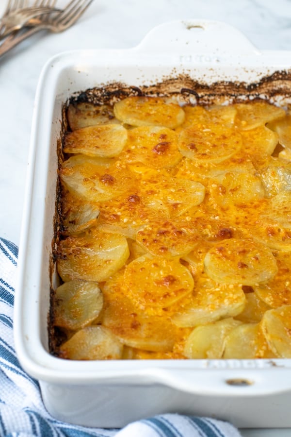 side view of a white casserole dish full of freshly made Au Gratin potatoes