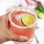 Pinterest Pin with title of recipe Hibiscus Margaritas and a photo of a hand holding a pink margarita