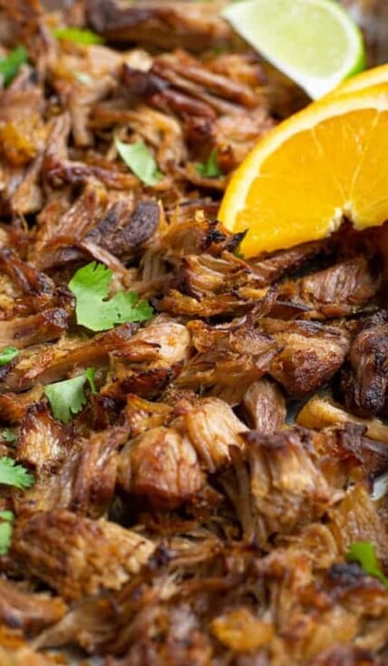 close up photo showing crispy carnitas on a sheet pan with an orange slice