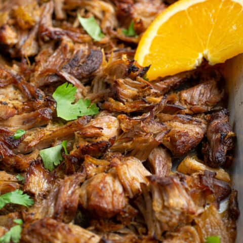 close up photo showing crispy carnitas on a sheet pan with an orange slice
