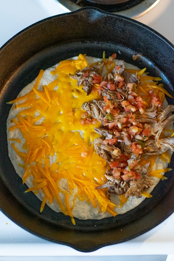 tortilla in a large skillet with melting cheese, carnitas, and fresh tomato salsa