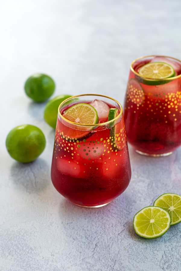 two glasses full of bright red Hibiscus Iced Tea Sparkler with ice and lime wedges