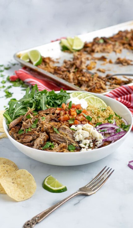 a carnitas bowl featuring a base of leftover carnitas, quinoa, and arugula with fresh topping make an excellent fast meal