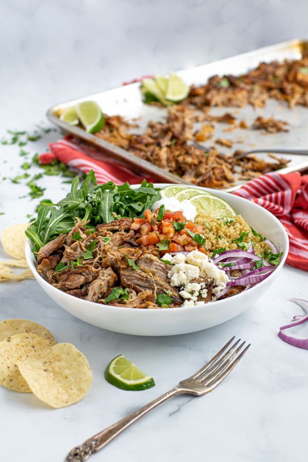 a carnitas bowl featuring a base of leftover carnitas, quinoa, and arugula with fresh topping make an excellent fast meal