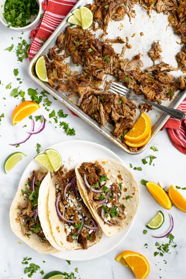 a sheet pan of carnitas next to a plate of pork carnitas tacos