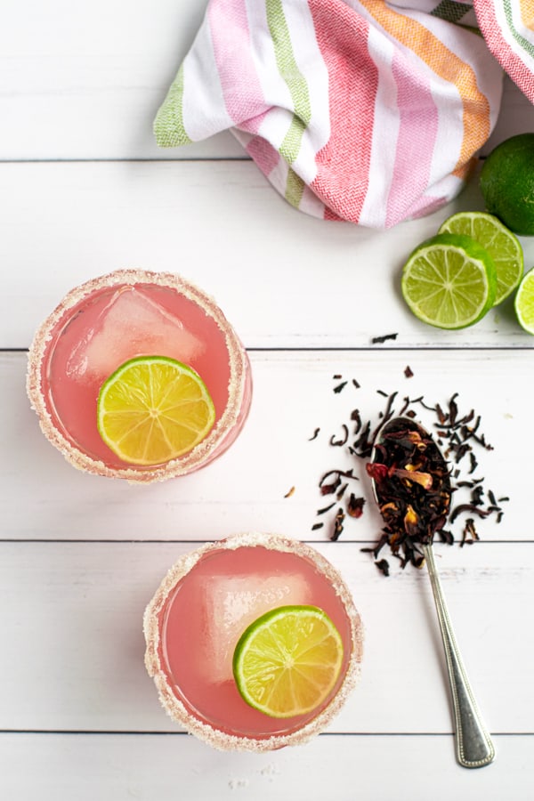 two bright pink hibiscus margaritas shot from above with a colorful towel and dried hibiscus tea