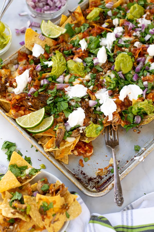 a fork on a sheet pan full of carnitas nachos pulling some off onto a plate
