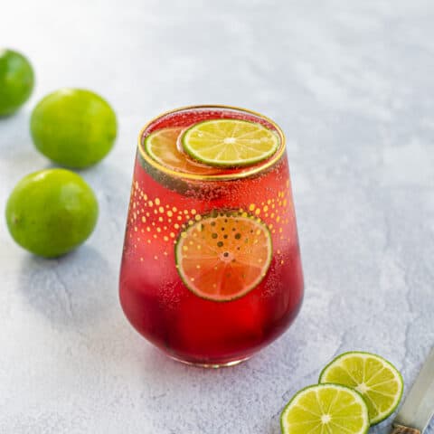 single glass of Hibiscus Iced Tea Sparkler with ice and a lime wedge