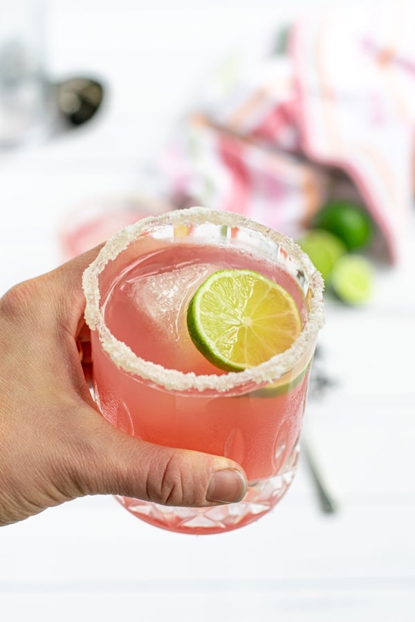 hand holding a glass of hibiscus margarita with a lime slice